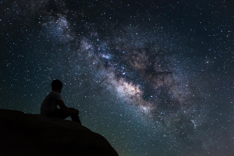 A photo of a man sitting in front of the milky way.